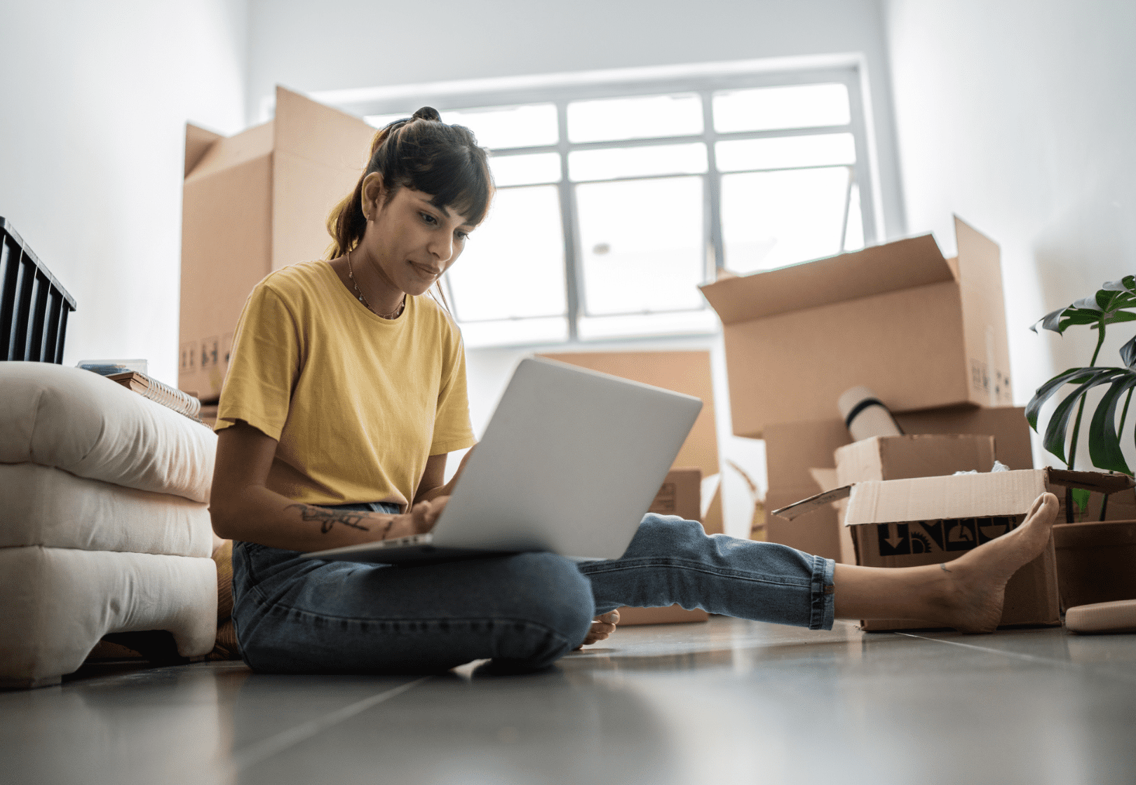 Woman sitting on ground with computer surrounded by moving boxes